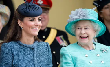Two women smiling at a public event, both wearing hats and formal attire.