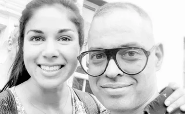 A woman smiles with a man wearing glasses in a black and white photo.