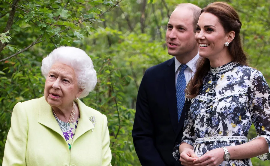 Three people standing outdoors, two smiling, with greenery in the background.
