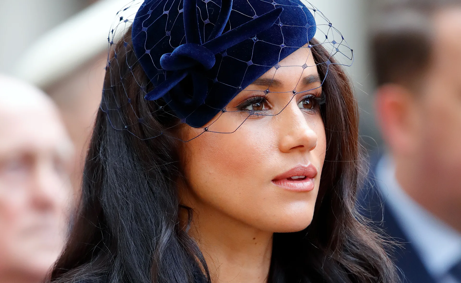 Close-up of a woman wearing a blue hat with netting, looking to the side with a neutral expression.