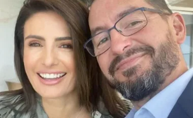 A smiling woman with dark hair and a bearded man with glasses taking a close-up selfie indoors.