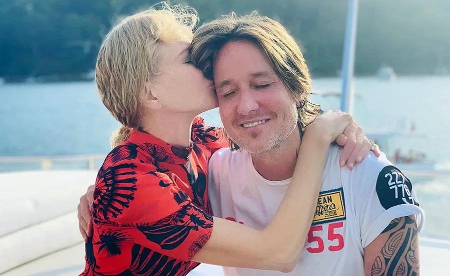 Woman in red kisses a smiling man on a boat with water in the background.