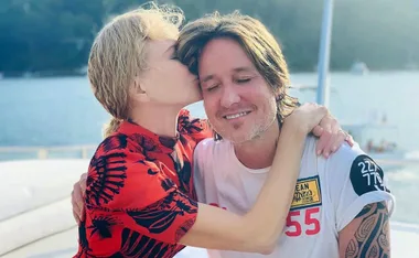 Woman in red kisses a smiling man on a boat with water in the background.