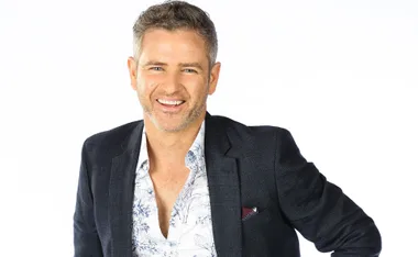 Man smiling in a suit with a floral shirt, white background.