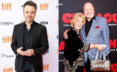 Man in a suit at TIFF event next to a smiling couple embracing at a red carpet event.