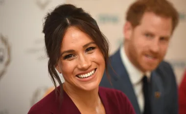 Smiling woman in maroon top at event, man in blue suit blurred in background.