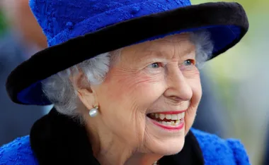 Elderly woman smiling warmly, wearing a blue hat with pearl earrings.