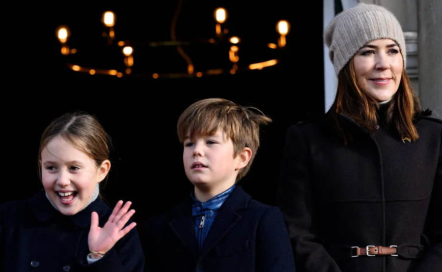 Princess Mary with twins Josephine and Vincent smiling and waving under a chandelier.