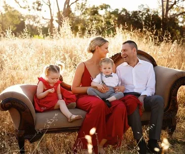 Family sitting on a couch in a field; parents in red and white, two children in red outfits.