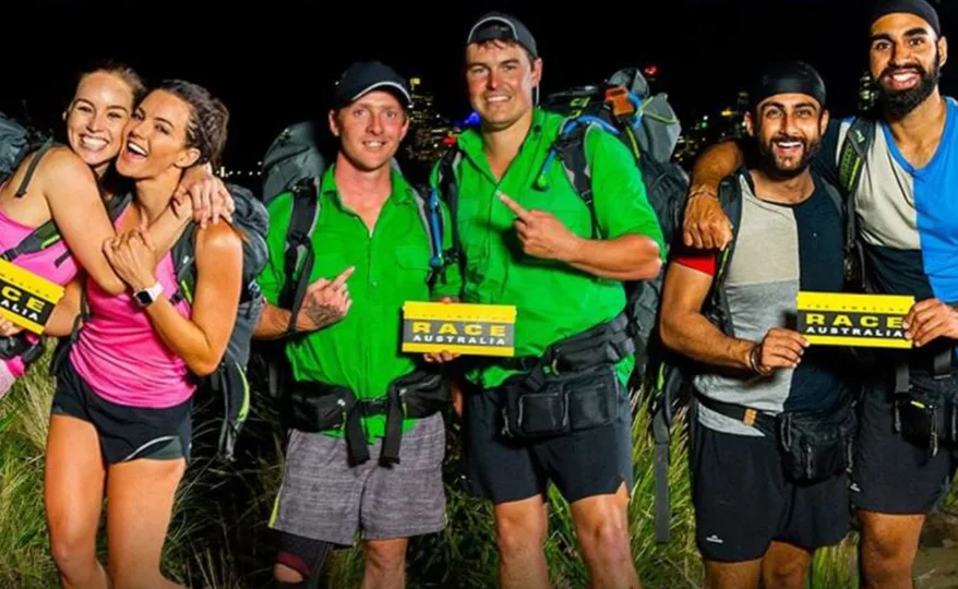 Contestants from The Amazing Race Australia 2022 with race cards, standing in outdoor nighttime setting.
