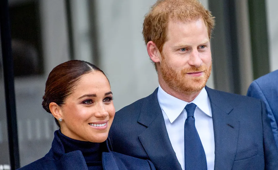 Prince Harry and Meghan Markle smiling, both wearing formal attire during a public appearance.