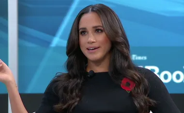 A woman speaking on stage with a microphone, wearing a black top with a red poppy pin.