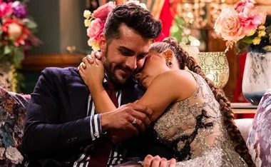 A couple embraces on a floral couch, surrounded by vibrant flowers and ornate decor.