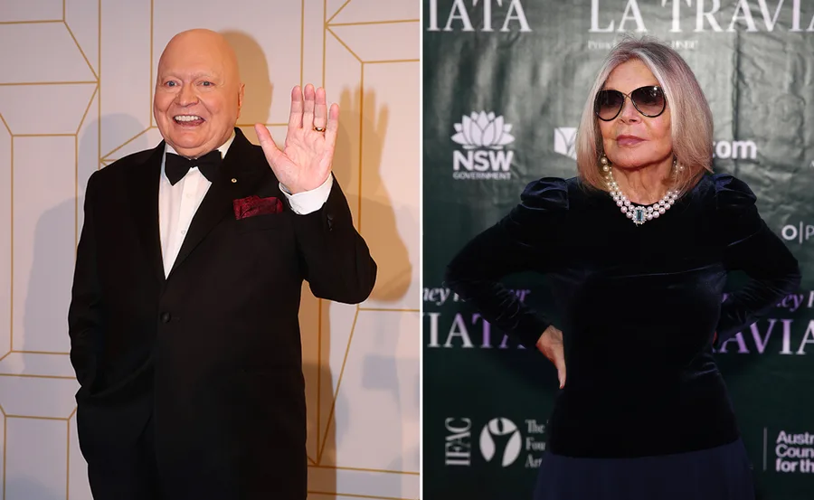 Man in tuxedo waving and woman in sunglasses posing confidently against event backdrop.
