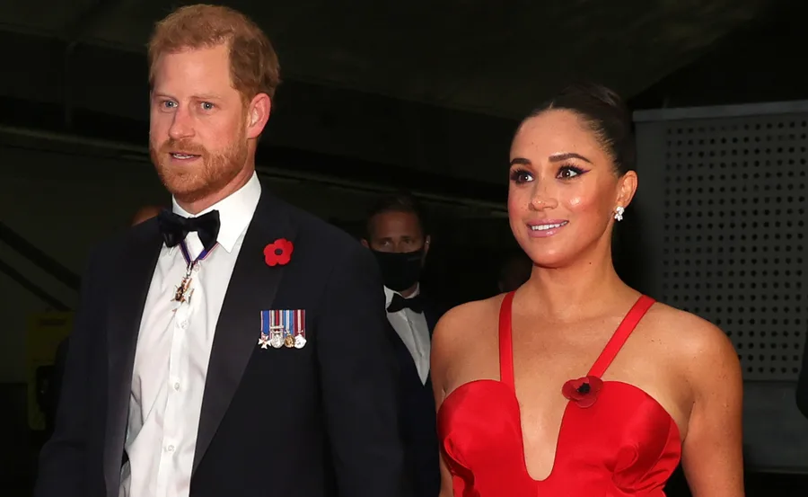 A man in a suit with medals and a woman in a red dress, both wearing poppies on their outfits at an event.