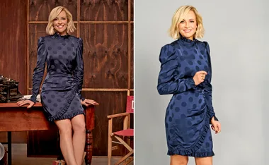 Blonde woman in a blue polka dot dress posing in a studio, smiling at the camera.