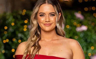 A person in a red off-shoulder dress, smiling, with warm lighting and bokeh effect in the background.