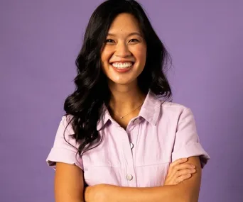 Smiling woman with long dark hair in a lavender shirt against a purple background.