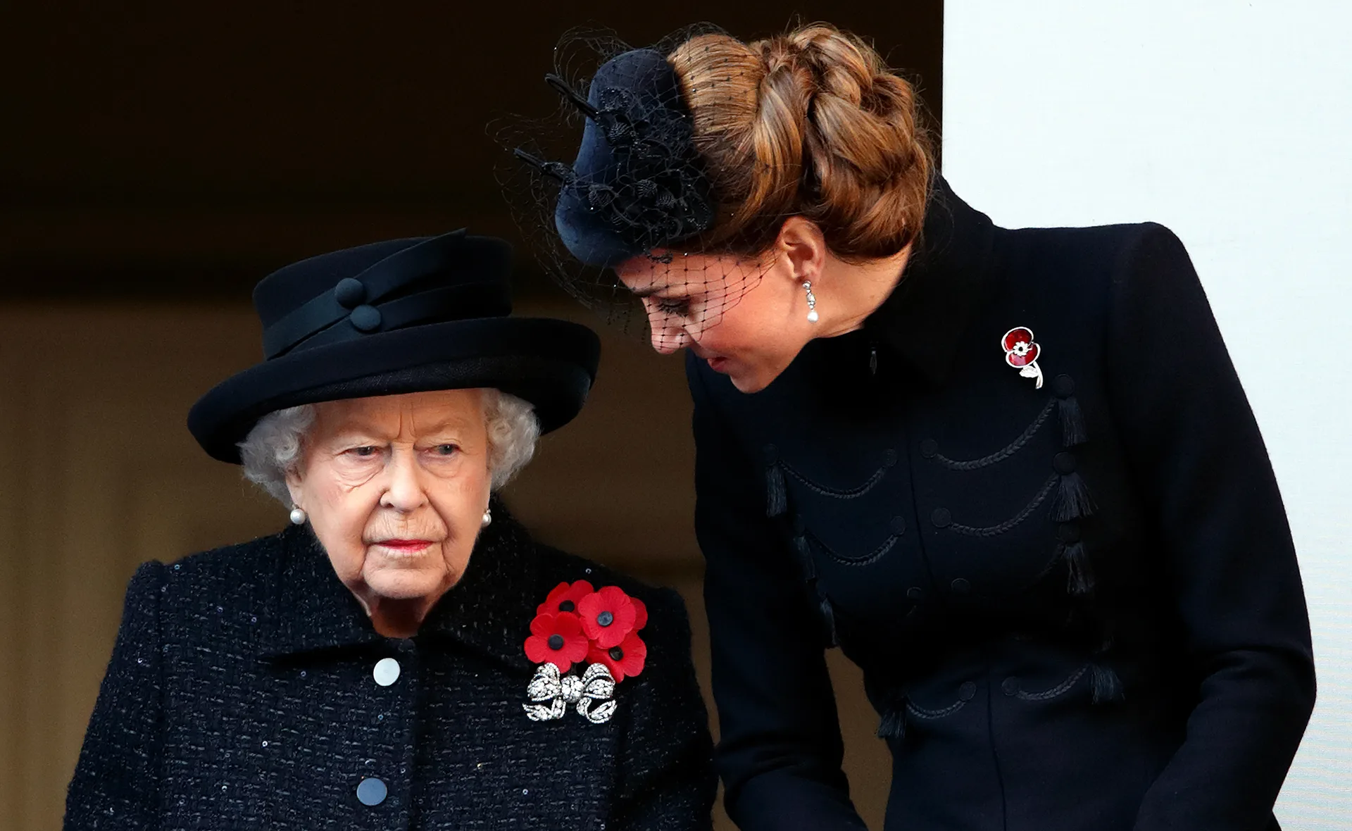 Two women in black attire with poppy pins stand together at a Remembrance Day service.