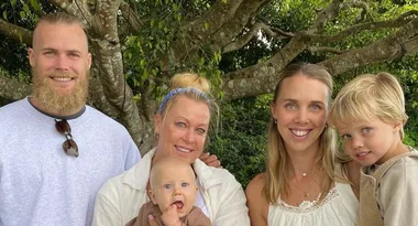 A family of five poses happily under a tree, including a newborn baby and a young child.