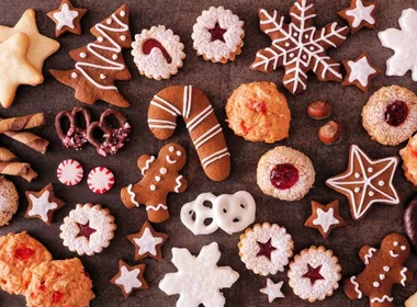 Assorted festive cookies and treats, including gingerbread, star shapes, and candy canes on a dark surface.