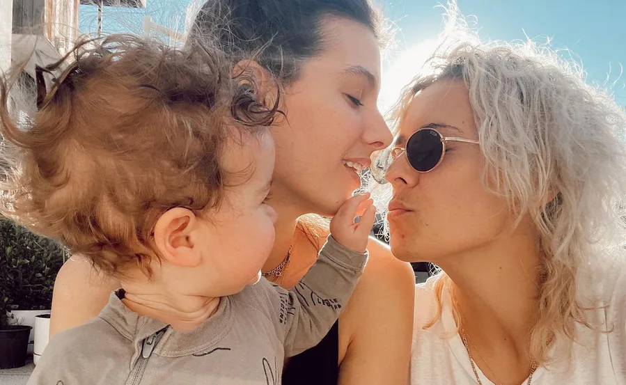 A family moment with two adults and a child, one adult is pregnant, sharing an affectionate outdoor scene.