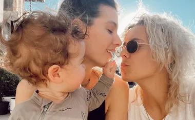 A family moment with two adults and a child, one adult is pregnant, sharing an affectionate outdoor scene.