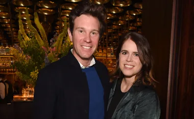 A couple smiling together at an indoor event with elegant decor in the background.