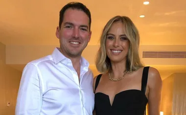 A couple smiling at a birthday celebration; woman in a black dress, man in a white shirt.