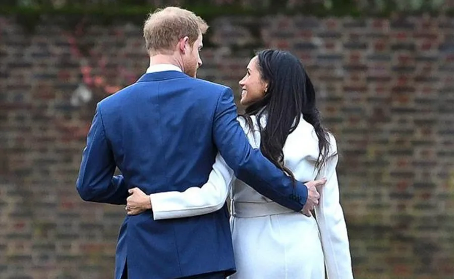 Couple walking away, embracing with arms around each other, in formal attire against a brick wall background.
