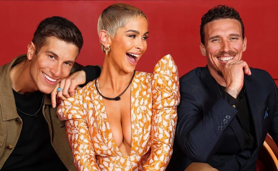 Three people smiling and posing against a red background, one wearing an ornate orange dress.