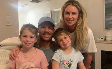 A family of four smiles in a cozy room with drawings and framed art on the walls.