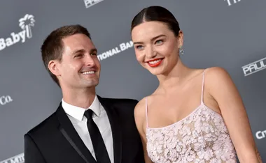 A couple smiling on a red carpet event, dressed in formal attire.