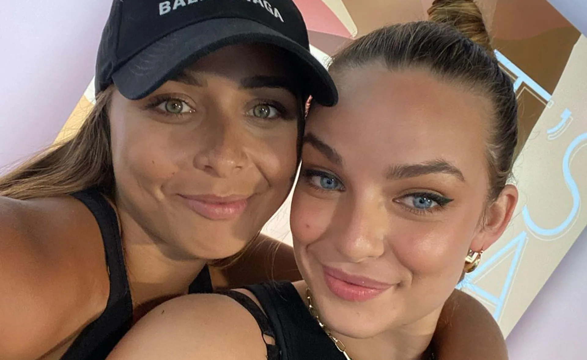Two women smiling; one wearing a cap, the other with a bun, in close embrace.
