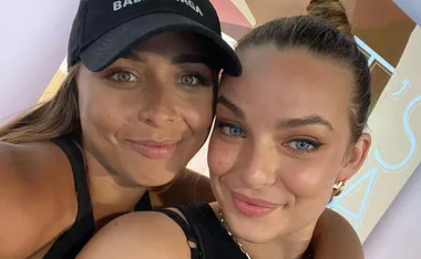 Two women smiling; one wearing a cap, the other with a bun, in close embrace.