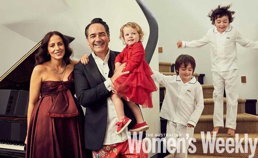 Family posing together in formal attire and pajamas near a stairway and piano, smiling for a holiday photo.