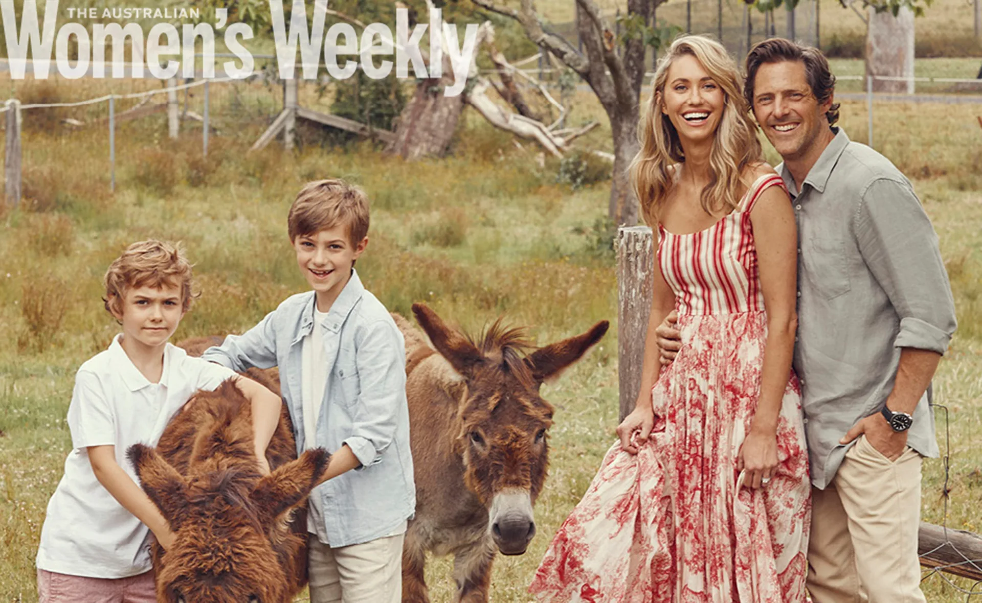 Family posing in a field with two small donkeys, smiling warmly at the camera.
