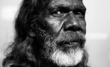 Close-up black and white portrait of an older man with long hair and a beard, looking thoughtfully into the distance.