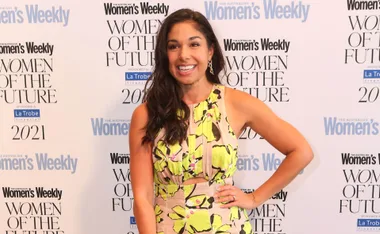 Woman in floral dress smiling at 'Women of the Future' event backdrop.