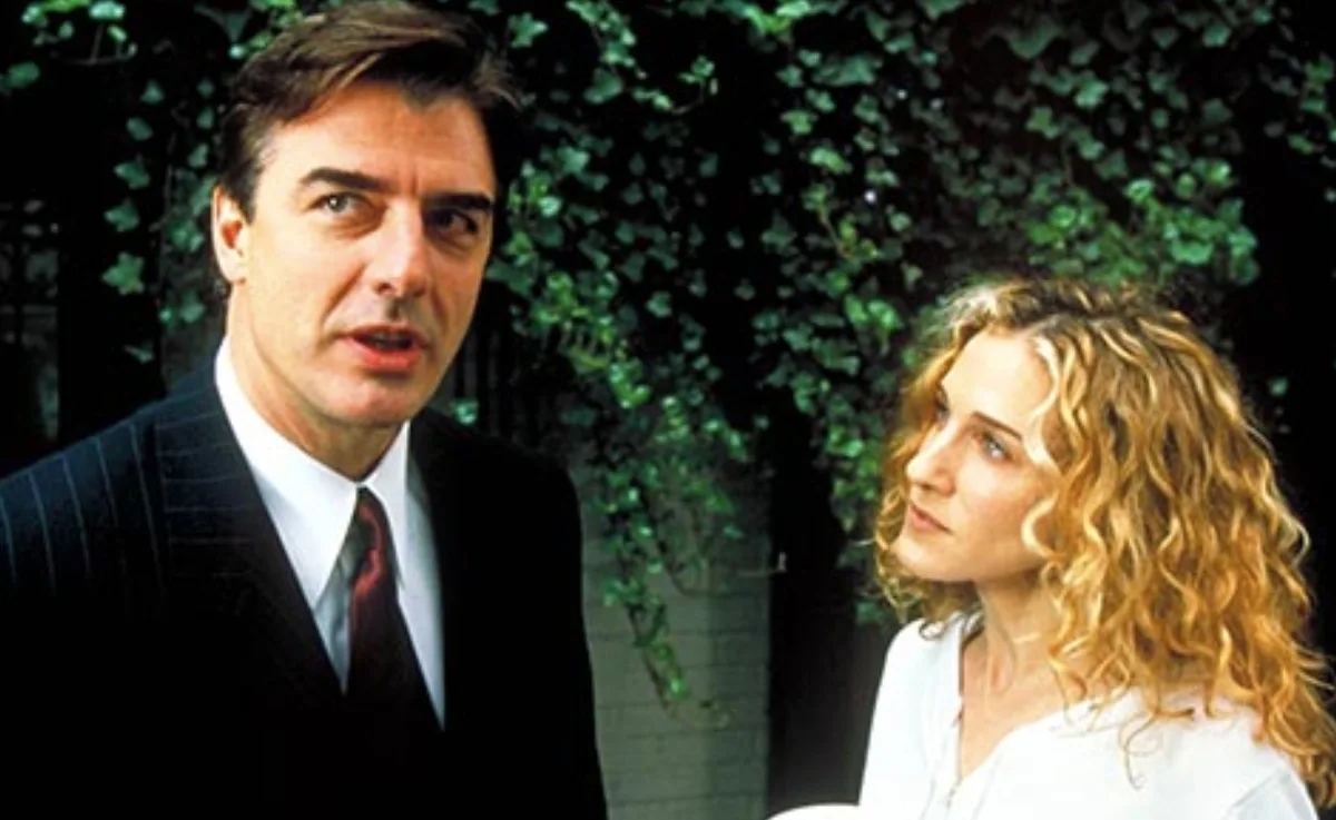 Man and woman talking outside with greenery in the background; the scene suggests a serious conversation.