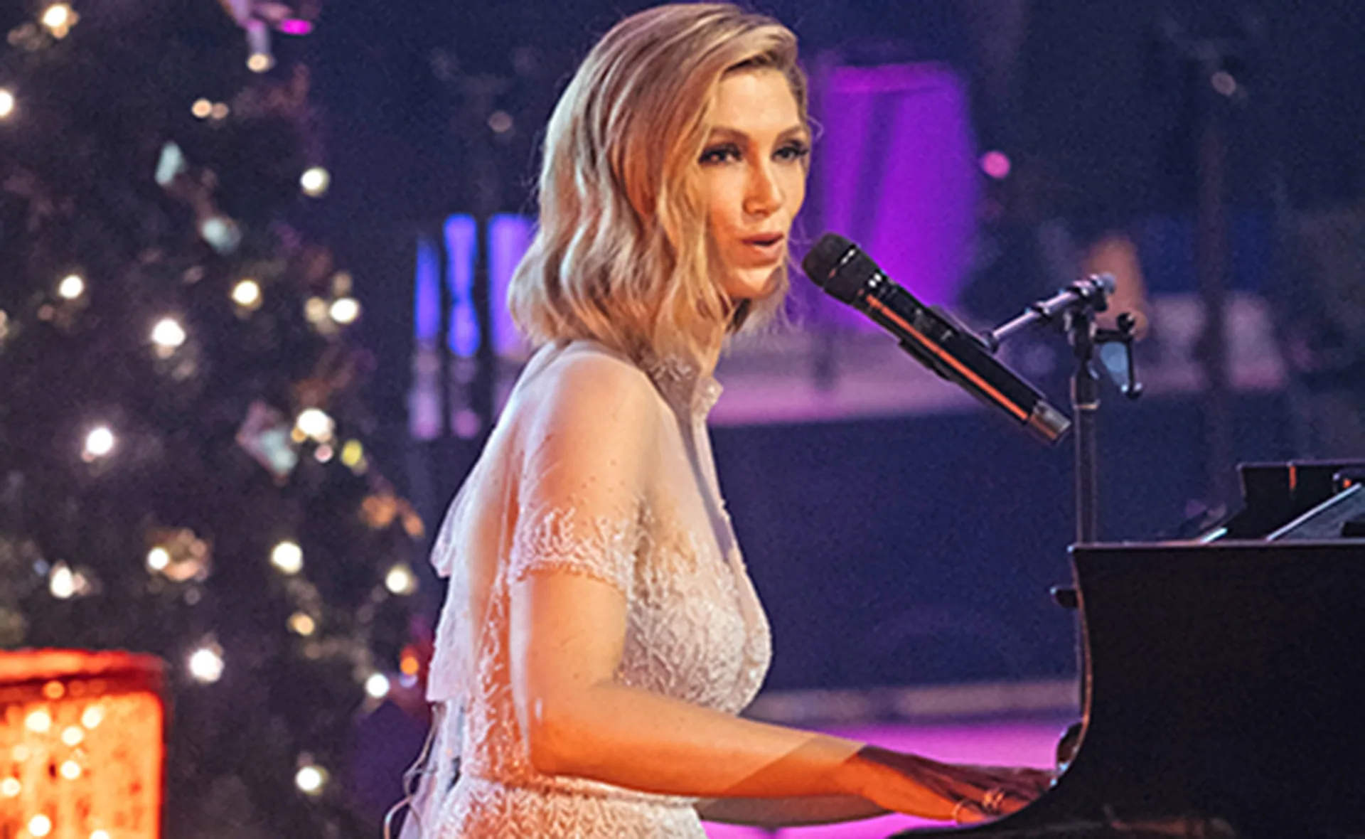 Singer performing at a piano on a festive stage with Christmas decorations.