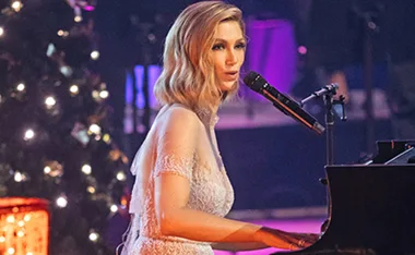 Singer performing at a piano on a festive stage with Christmas decorations.