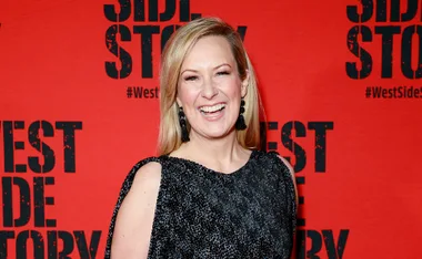 Blonde woman in a black dress smiles in front of a red "West Side Story" backdrop.
