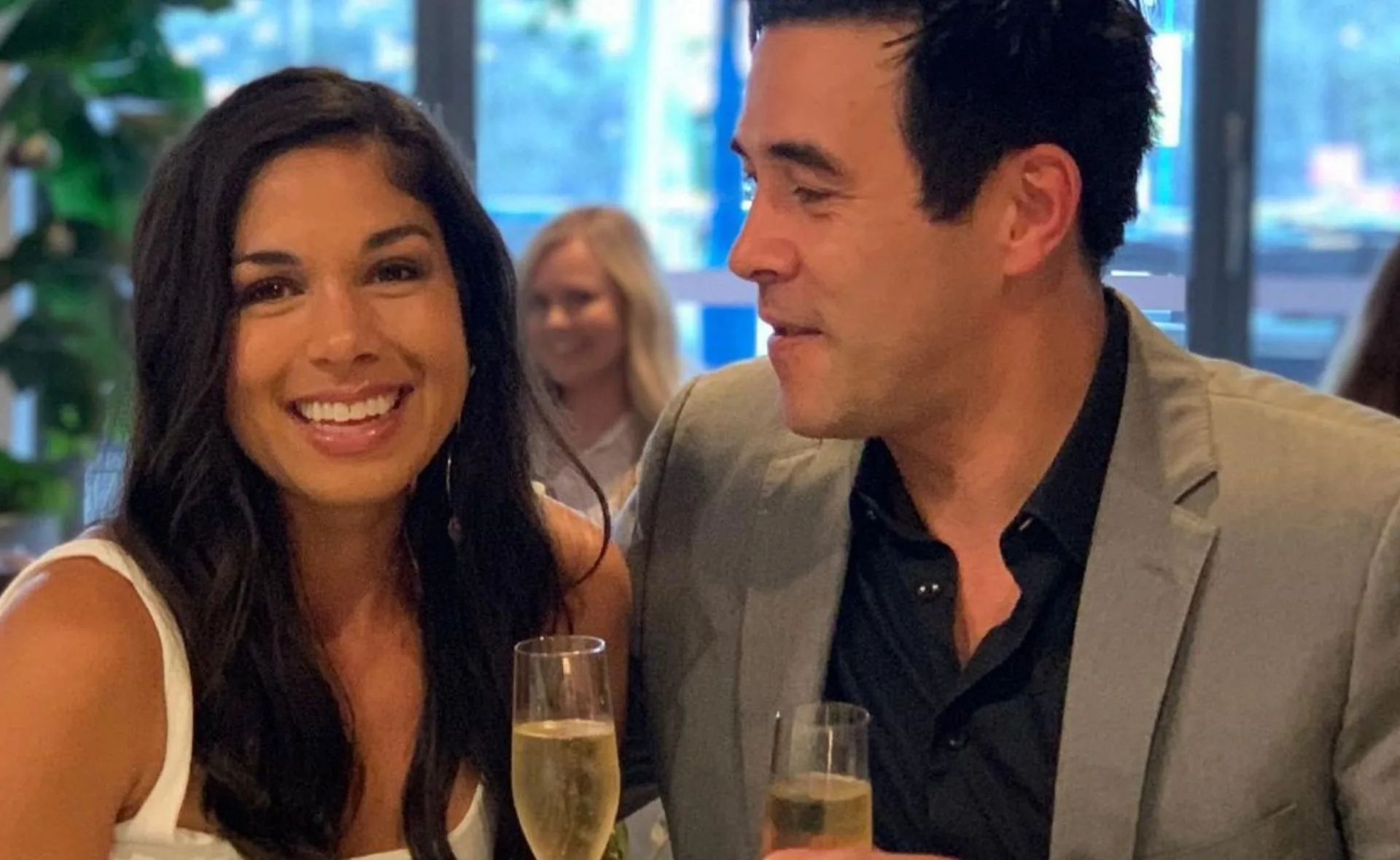 Two people smiling and holding champagne glasses in a social setting.