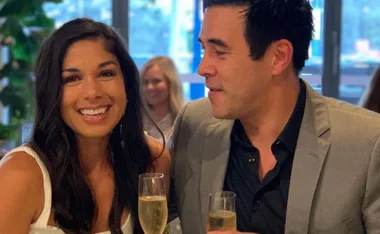 Two people smiling and holding champagne glasses in a social setting.