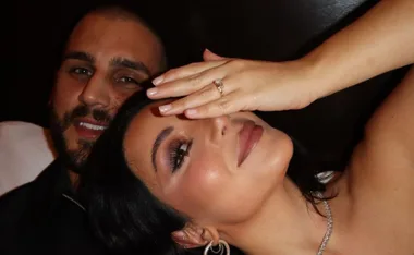 Couple smiling, woman covering face showing an engagement ring.