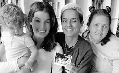Four people smiling, one holding a child and another holding a sonogram photo, seated in front of a bookshelf.