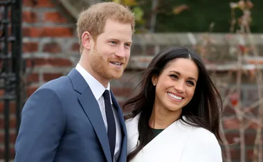 Prince Harry and Meghan Markle smiling outdoors, standing closely together.