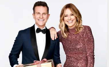 Two people dressed formally, one holding a wrapped gift, smiling together.