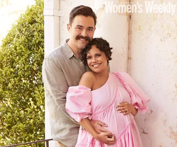 Couple embracing, the woman in a pink dress smiles, holding her baby bump beside a man in a light shirt. "Women's Weekly" header.